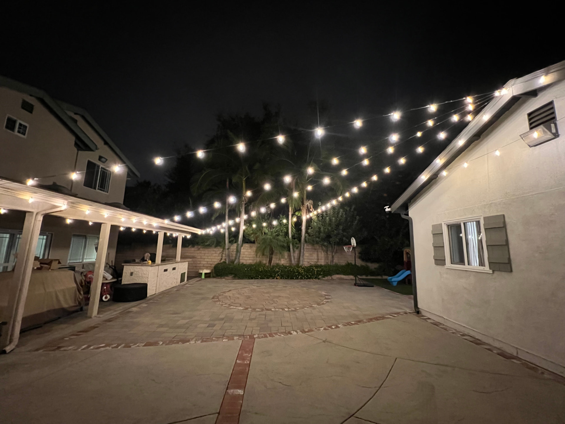 Backyard patio at night with string lights crisscrossing above paved seating area